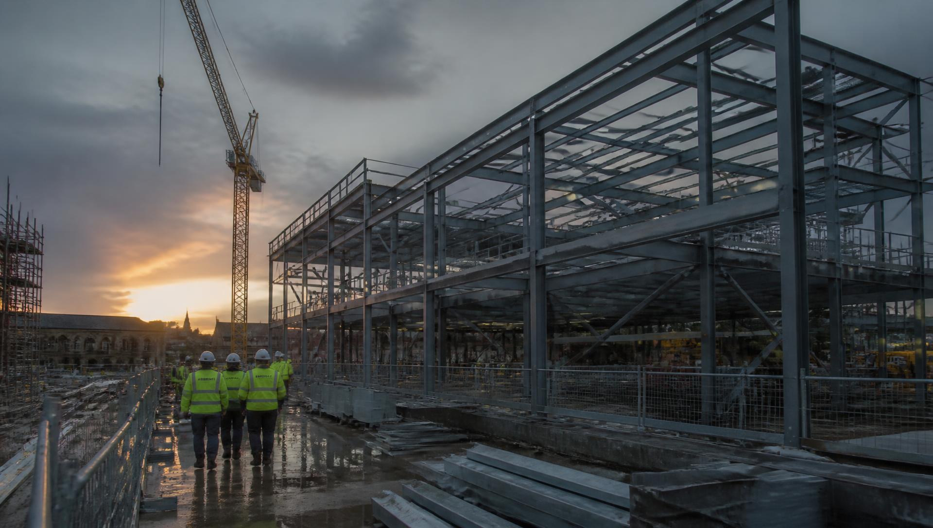Commercial construction site with steel frame and tower crane at dusk